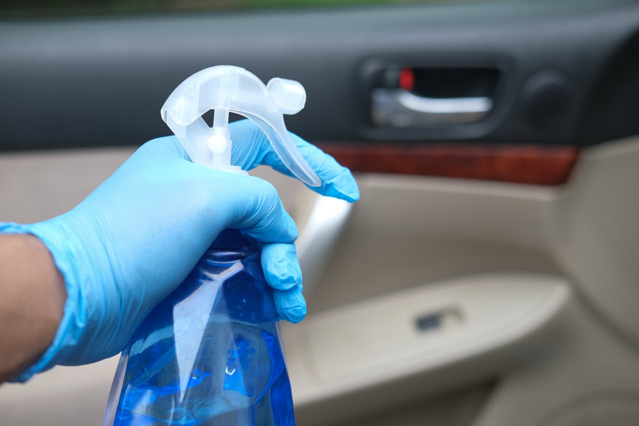 Close-up of a gloved hand holding a blue spray bottle for cleaning a car interior.